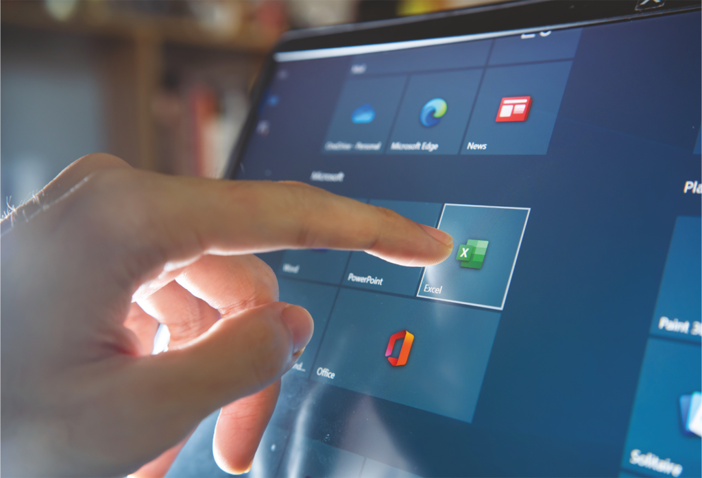 A finger pointing to microsoft excel on a monitor.