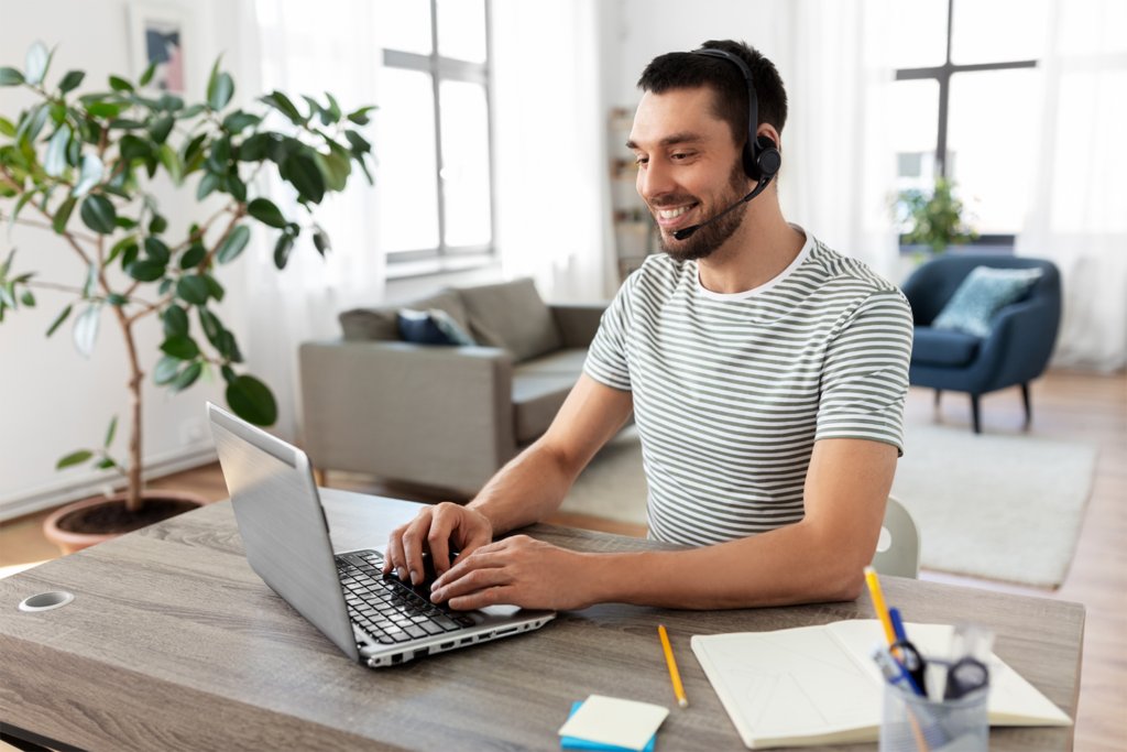 An image of a man smiling and working on a laptop with a headset and a headset.